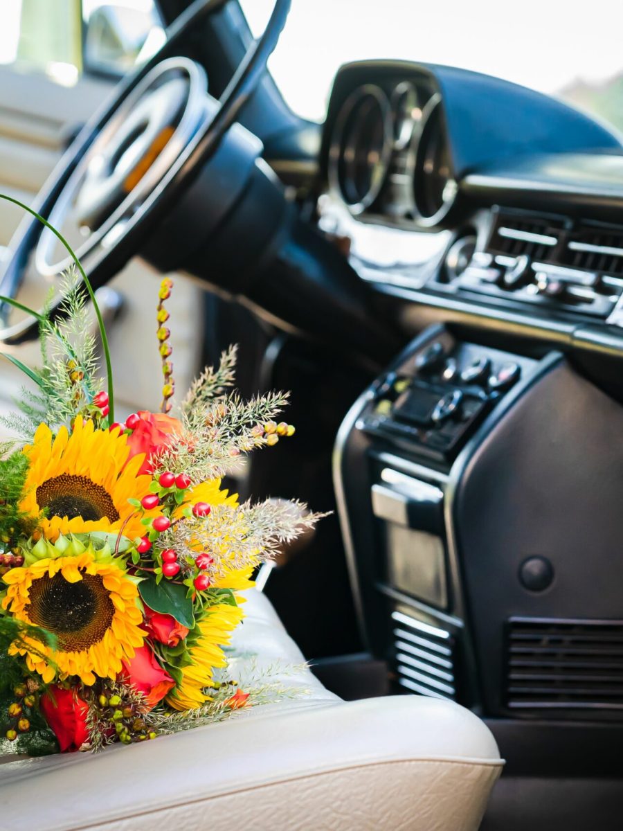 A vibrant sunflower wedding bouquet is placed on the passenger seat of a car.